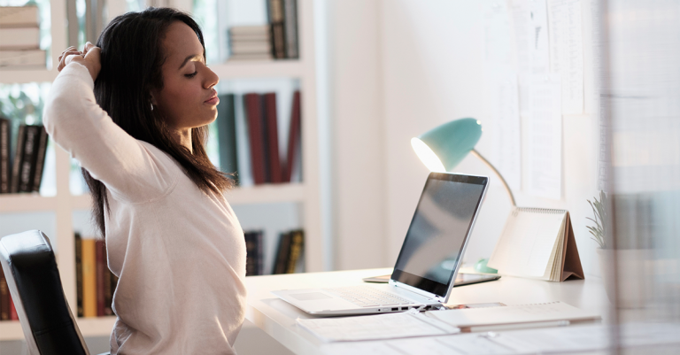 Female stretching arms behind her at office workstation