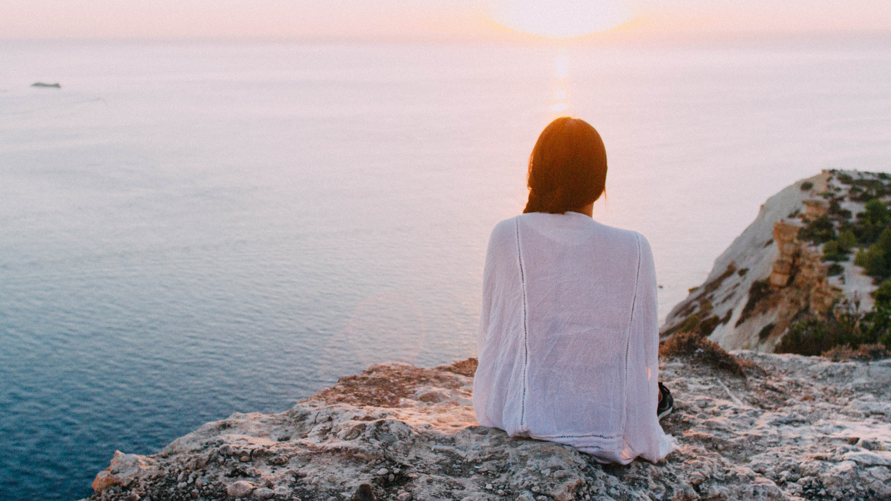 Woman sitting on rocks looking at the ocean