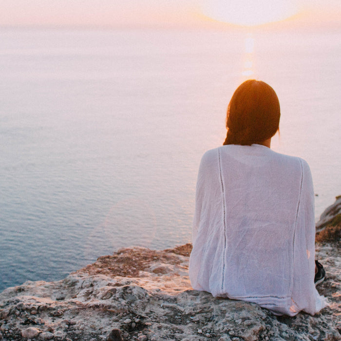 Woman sitting on rocks looking at the ocean