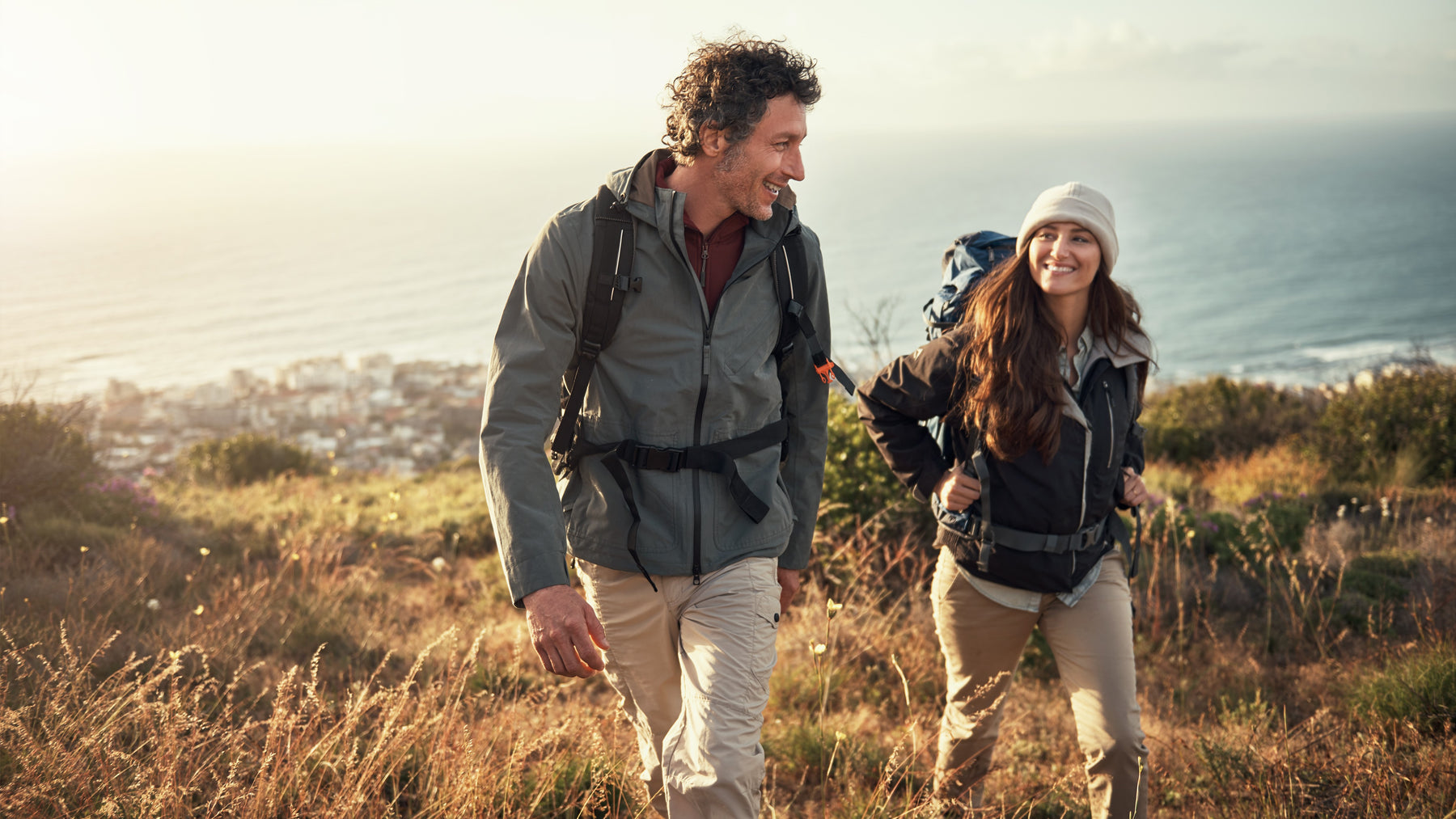 A man and woman hiking on a mountain with the ocean in the background