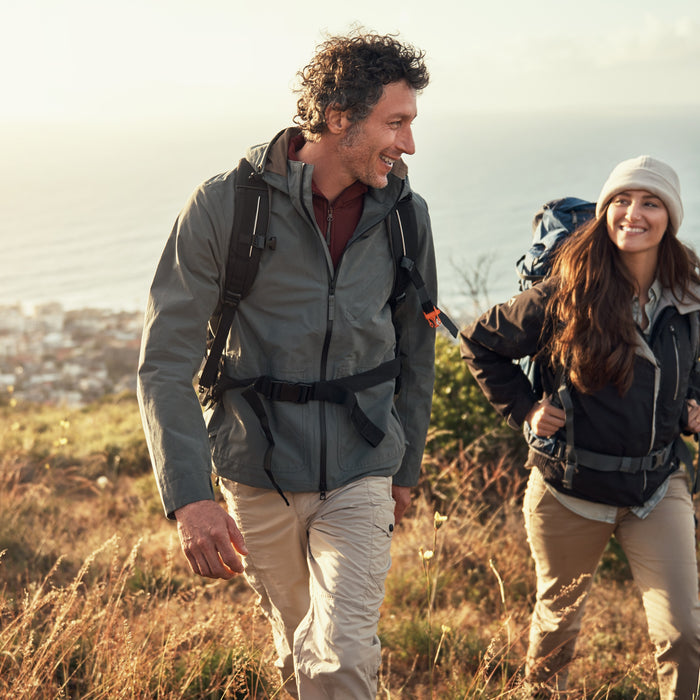 A man and woman hiking on a mountain with the ocean in the background