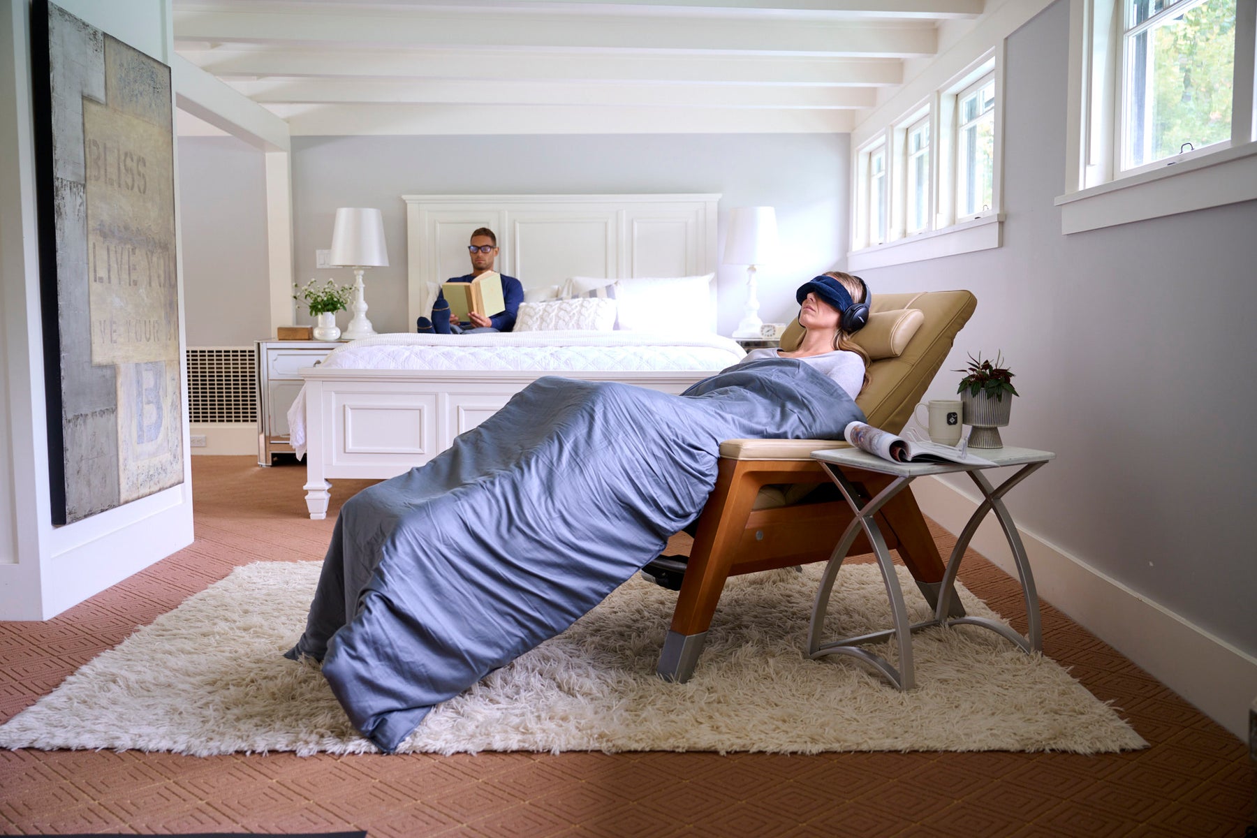 A woman reclining in the Gravis Zero Gravity Recliner with a weighted blanket and Tempur sleep mask