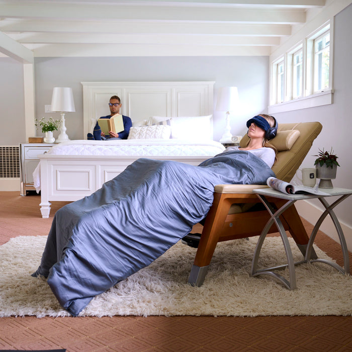 A woman reclining in the Gravis Zero Gravity Recliner with a weighted blanket and Tempur sleep mask