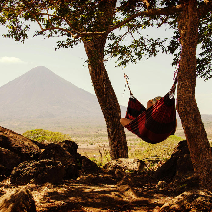 Person Lying on Black and Red Hammock Beside Mountain Under White Cloudy Sky during Daytime