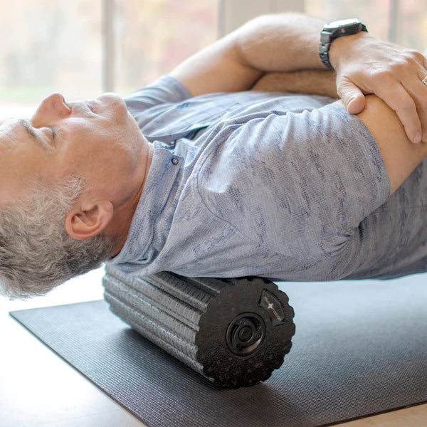 A man in a blue shirt using the Rollvibe Max Vibrating Massage Roller on his back.