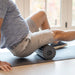 A man in a blue shirt and khaki shorts using the Rollvibe Max Vibrating Massage Roller on his leg.